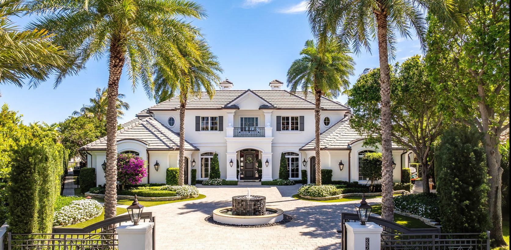 White two-story home with a palm-lined motor court and fountain