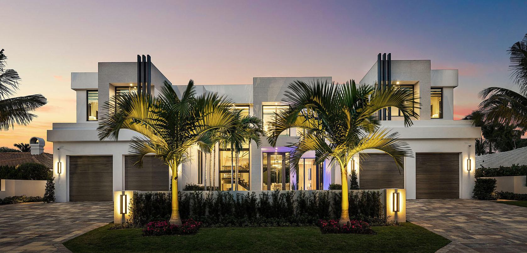 Modern home at sunset with uplit palms and a manicured hedge