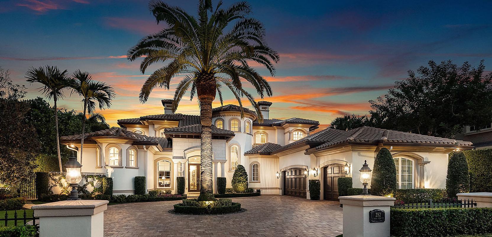 Mediterranean-style estate at sunset with palms and a paver drive