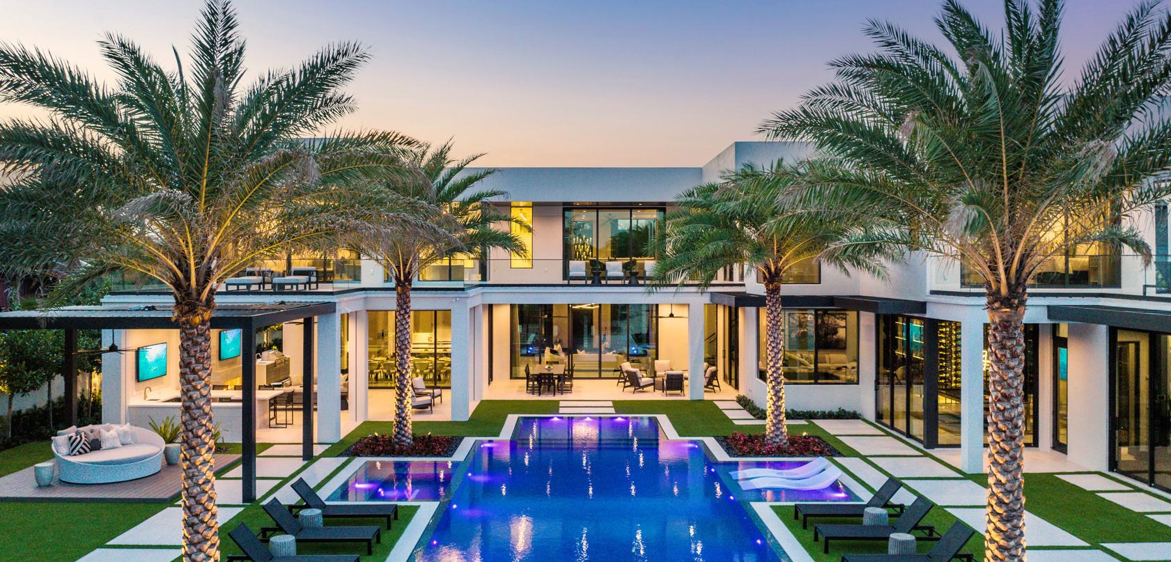 Modern home at dusk with palms around a lit pool